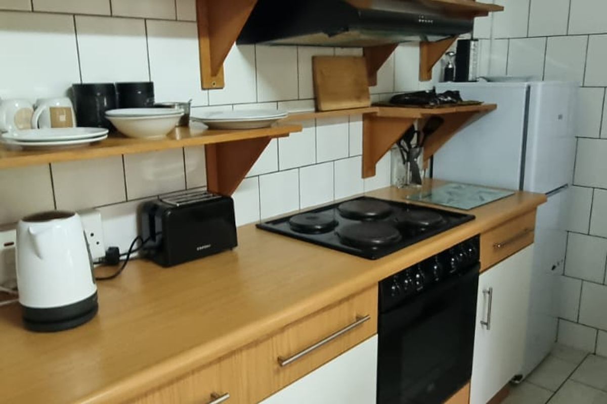 Functional kitchen featuring laminate countertops, built-in oven, electric hob, extractor fan, and open shelving with tiled backsplash and flooring.
