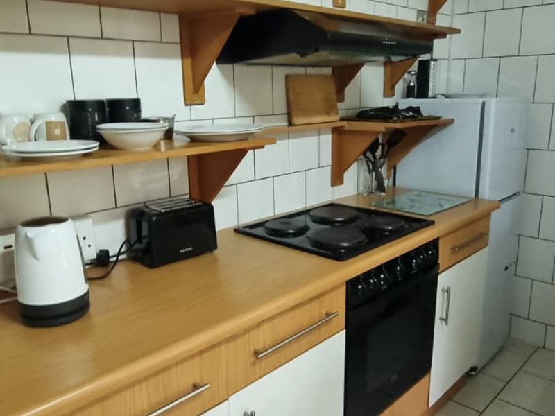 Functional kitchen featuring laminate countertops, built-in oven, electric hob, extractor fan, and open shelving with tiled backsplash and flooring.