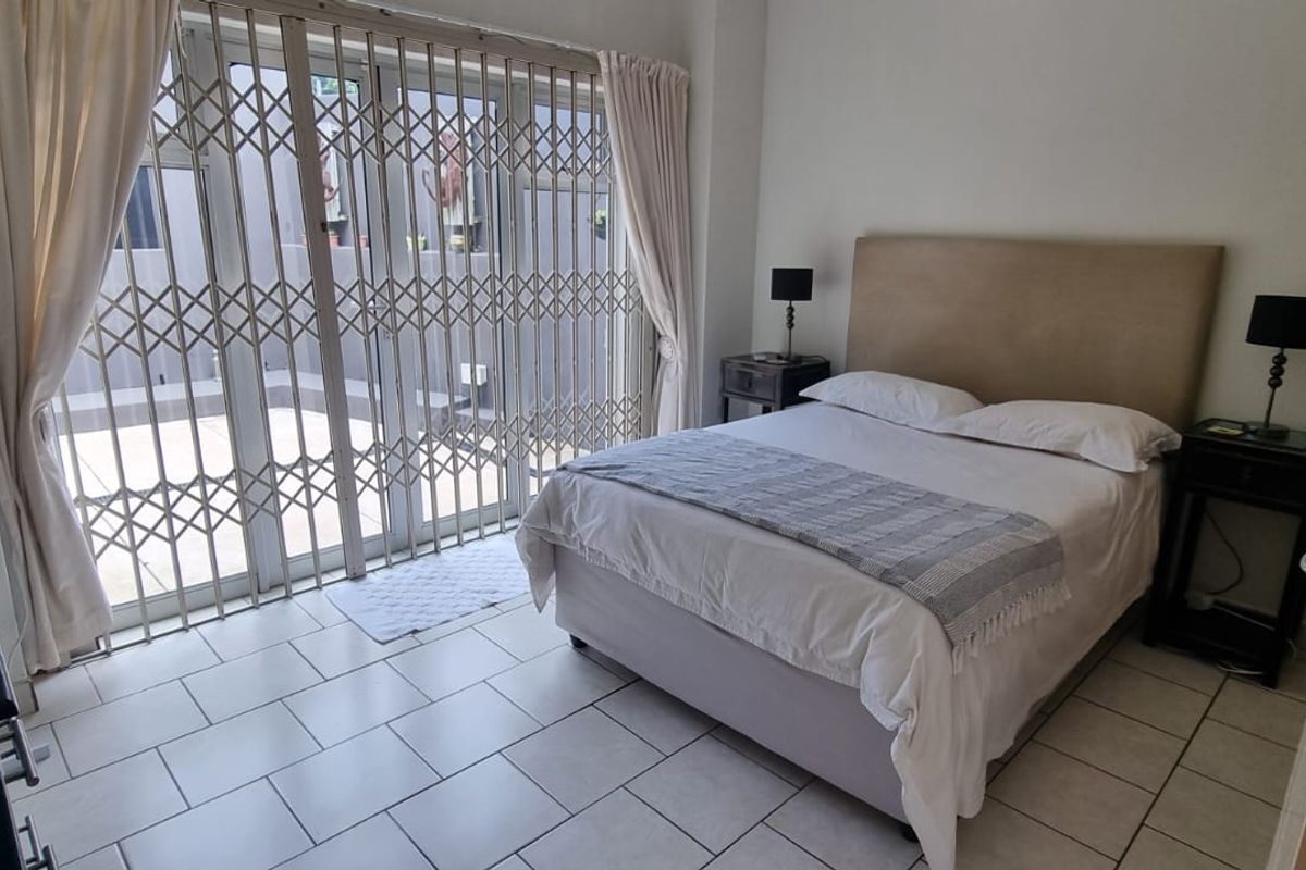 A bedroom featuring tiled flooring and a sliding glass door with a fitted metal security gate, providing direct access to an outdoor area.