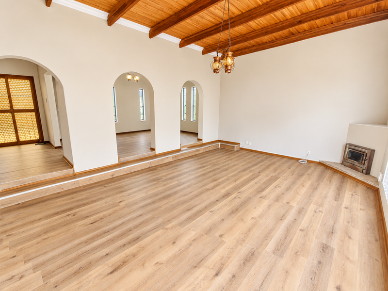 Spacious living area featuring exposed timber ceiling beams, laminate flooring, arched architectural details, and a built-in fireplace.