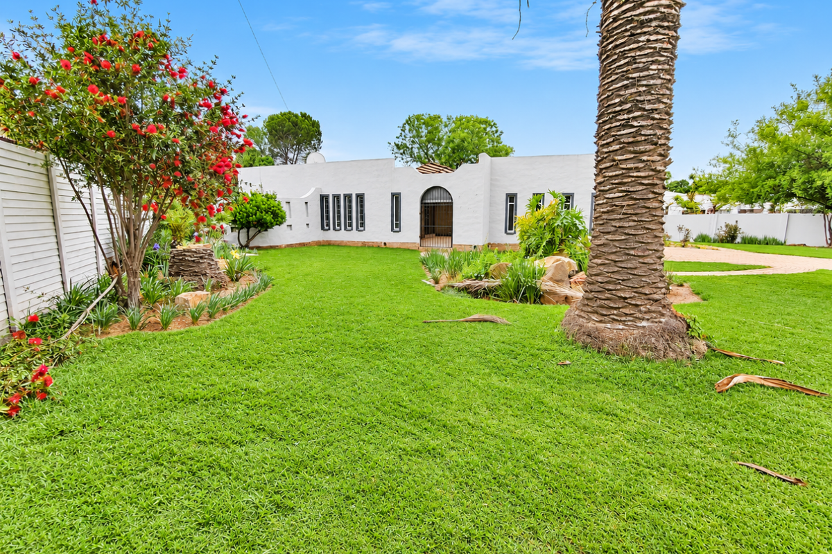 A well-maintained rear garden featuring a lush green lawn, mature palm tree, and established landscaping, providing a private outdoor space.