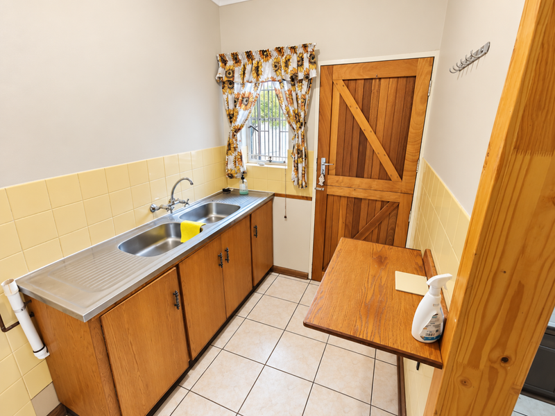 A functional laundry room featuring wooden cabinetry, a stainless steel double sink, tiled splashbacks, and a convenient folding wall-mounted table.
