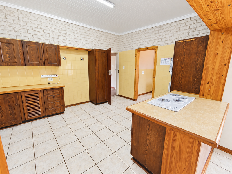 Spacious kitchen featuring wooden cabinetry, laminate countertops, a built-in electric hob, and neutral ceramic tiling throughout.