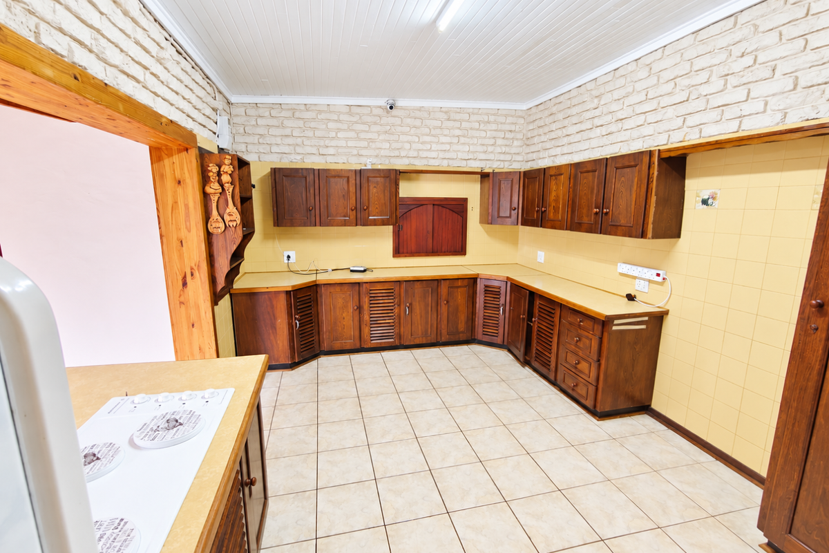 Spacious kitchen featuring extensive wooden cabinetry, laminate countertops, ceramic wall tiling, and a classic tongue and groove ceiling.