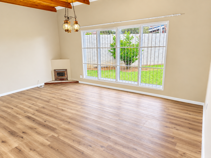 Spacious living room featuring modern laminate flooring, exposed timber ceiling beams, and a built-in fireplace with large windows overlooking the garden.