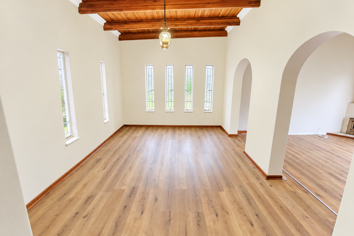 Spacious living area featuring exposed timber ceiling beams, warm laminate wood flooring, and elegant arched doorways leading to adjacent rooms.