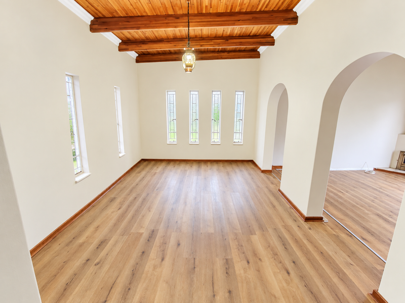 Spacious living area featuring exposed timber ceiling beams, warm laminate wood flooring, and elegant arched doorways leading to adjacent rooms.