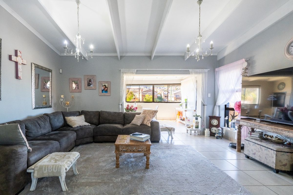 Spacious living room featuring a vaulted ceiling with exposed beams, tiled flooring, and large sliding doors leading to an adjoining patio area.