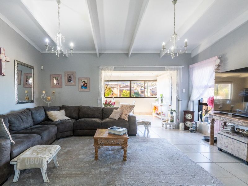 Spacious living room featuring a vaulted ceiling with exposed beams, tiled flooring, and large sliding doors leading to an adjoining patio area.