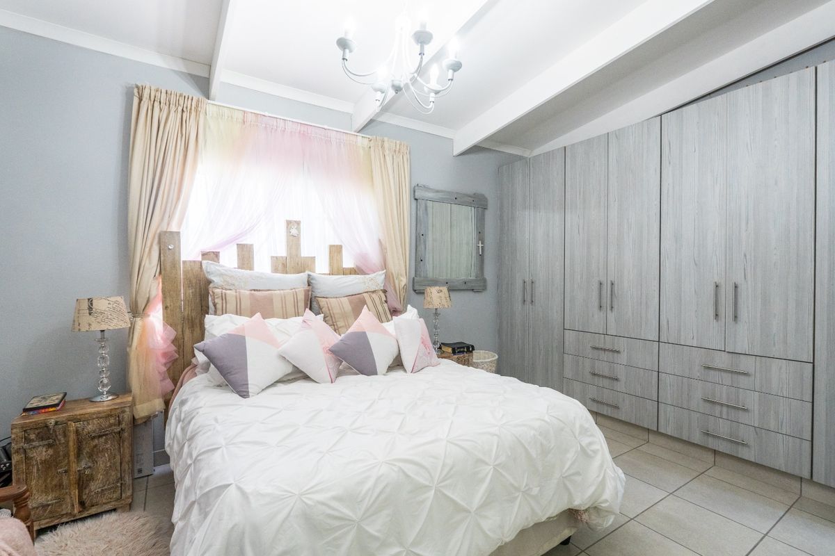 A well-maintained bedroom featuring built-in cupboards, tiled flooring, and exposed ceiling beams, providing a functional and comfortable living space.