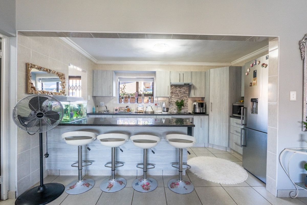 Functional kitchen featuring granite countertops, ample built-in cabinetry, a tiled backsplash, and a breakfast bar area with integrated sink and extractor fan.