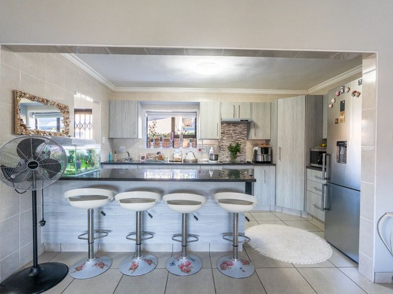 Functional kitchen featuring granite countertops, ample built-in cabinetry, a tiled backsplash, and a breakfast bar area with integrated sink and extractor fan.