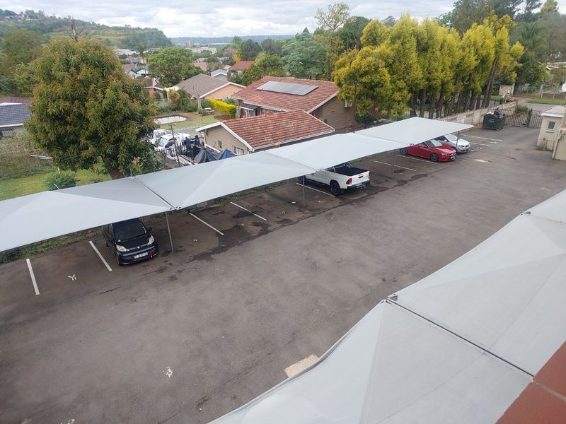 Aerial view of the apartment complex parking area featuring covered shade cloth carports and marked asphalt parking bays.