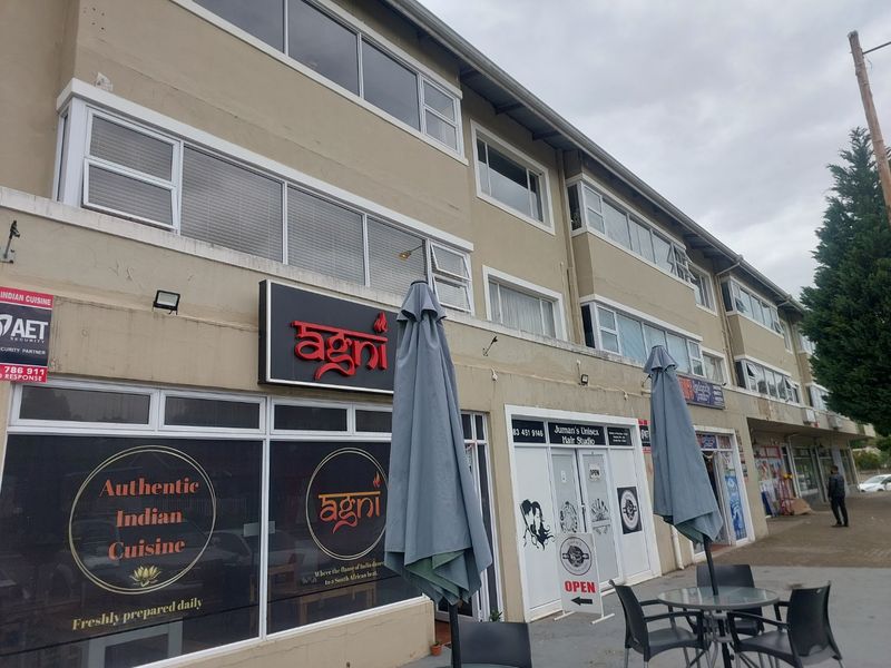 Exterior view of a multi-level apartment building featuring ground-floor commercial storefronts and upper-level residential windows.