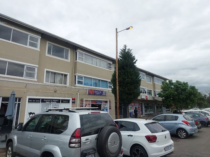 Exterior view of a multi-story apartment building featuring ground-floor commercial storefronts and parking area.