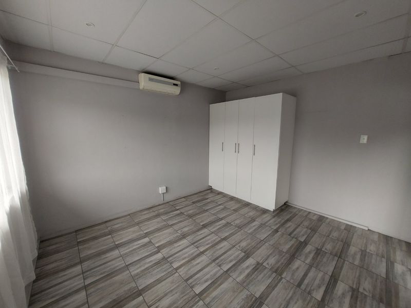 A clean, empty bedroom featuring tiled flooring, a built-in wardrobe, and a wall-mounted air conditioning unit.