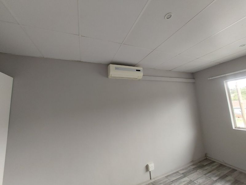 An empty bedroom featuring a drop ceiling with recessed lighting, laminate flooring, and a wall-mounted split-system air conditioner.