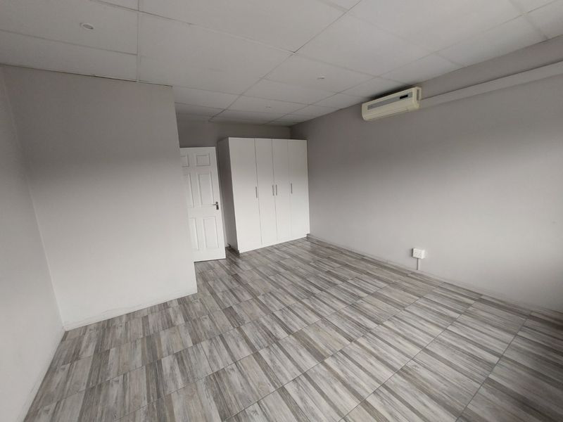 A clean, empty bedroom featuring modern wood-look tiled flooring, built-in cupboards, and a wall-mounted air conditioning unit.