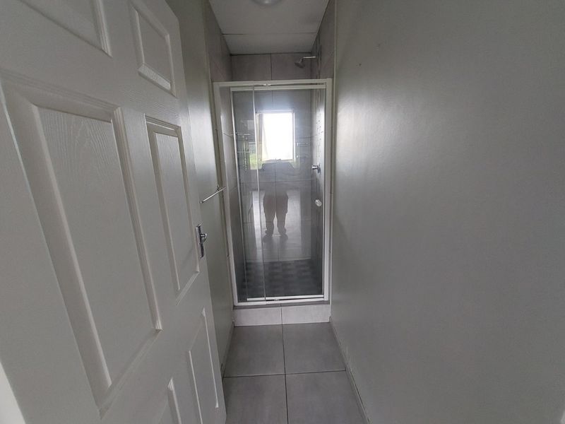 A compact bathroom featuring a glass-enclosed shower with tiled walls and flooring.