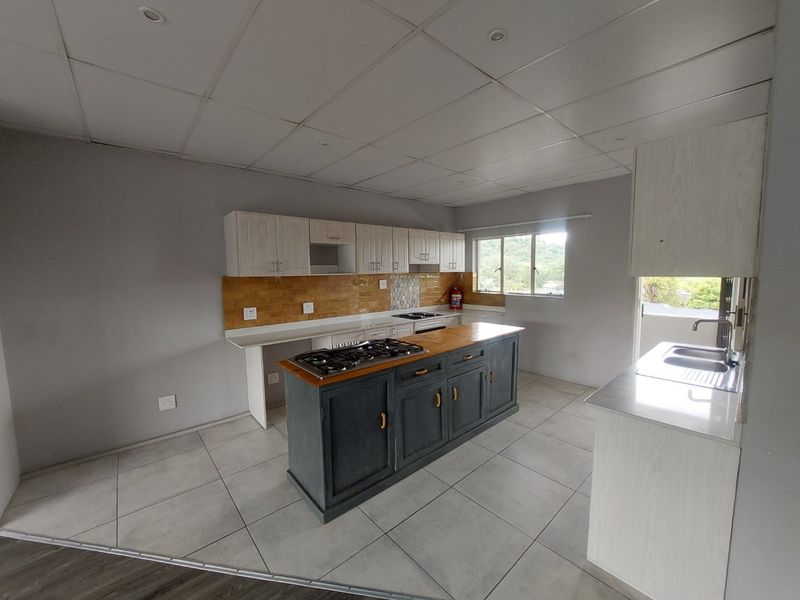 Spacious kitchen featuring a central island with a gas hob, ample built-in cabinetry, tiled backsplash, and large windows providing natural light.