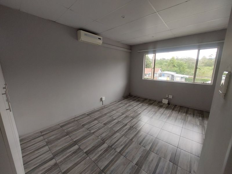 An empty bedroom featuring modern wood-look tiled flooring, a drop ceiling, and a wall-mounted air conditioning unit with a view of the exterior.
