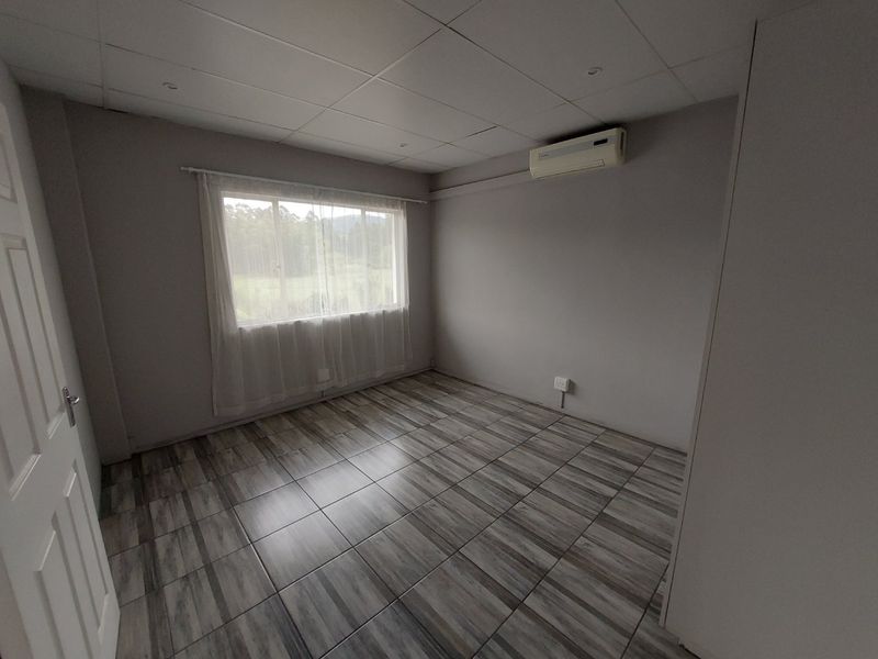 A clean, empty bedroom featuring tiled flooring, a drop ceiling, and a wall-mounted air conditioning unit.