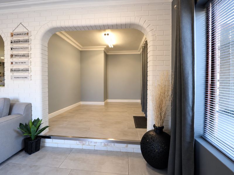 A bright, open-plan living area featuring a distinctive white brick arched entryway, neutral tiled flooring, and elegant crown molding.