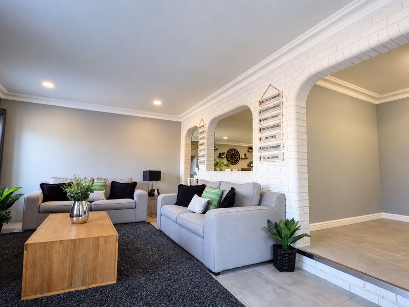 A well-maintained living room featuring a distinctive white brick archway, crown molding, recessed lighting, and neutral tiled flooring.