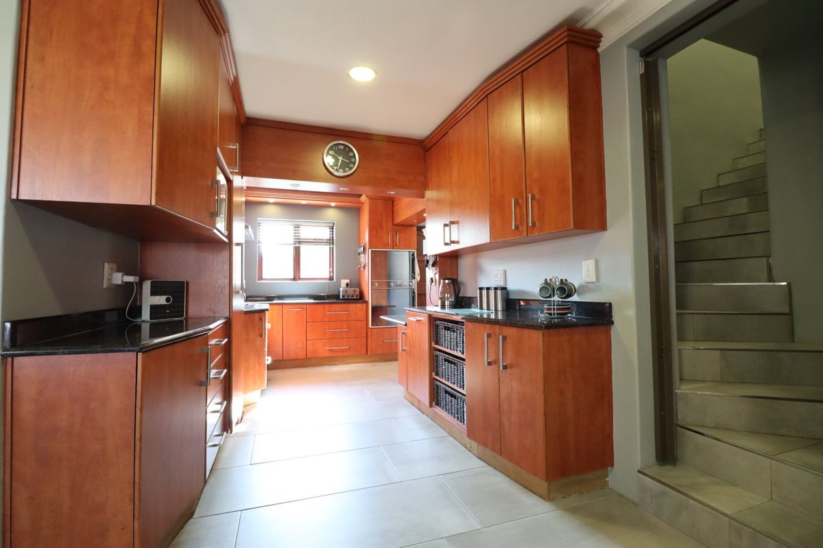 A well-maintained kitchen featuring warm-toned wooden cabinetry, granite countertops, built-in oven, and tiled flooring, with an adjacent staircase leading to another level.