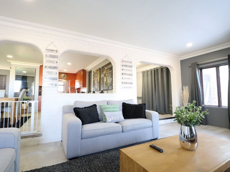 Open plan living area featuring distinctive white painted brick arched openings connecting to the kitchen and dining space with modern tiled flooring.