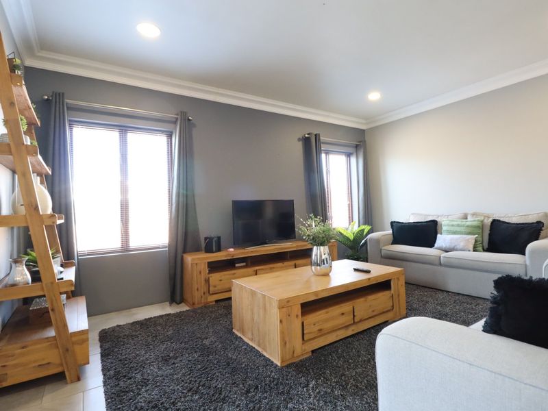 A well-maintained living room featuring neutral wall tones, crown molding, recessed downlights, and tiled flooring, offering a bright and comfortable living space.