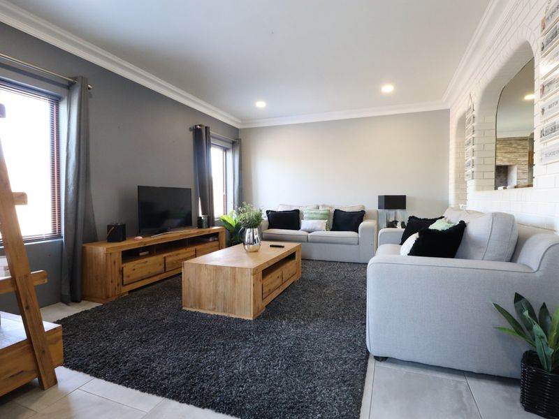 A well-maintained living room featuring tiled flooring, recessed downlighting, crown molding, and a distinctive white brick feature wall.