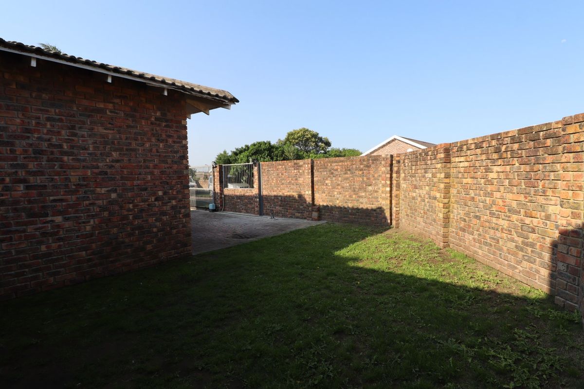 A private rear yard featuring a paved driveway, secure metal gate, and high face brick boundary walls surrounding a lawn area.