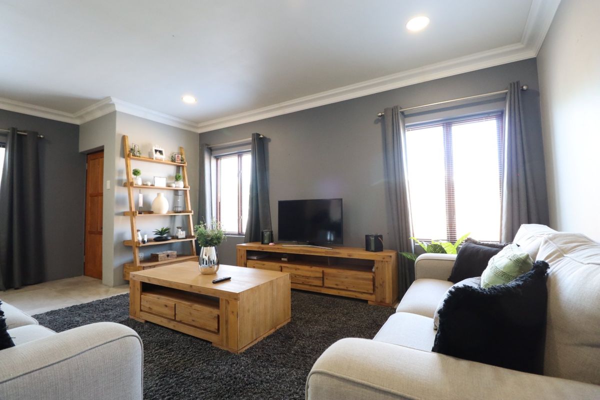A comfortable living room featuring crown molding, recessed downlighting, and large windows with venetian blinds, creating a bright and inviting space.
