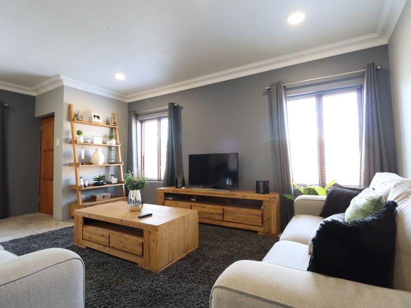 A comfortable living room featuring crown molding, recessed downlighting, and large windows with venetian blinds, creating a bright and inviting space.