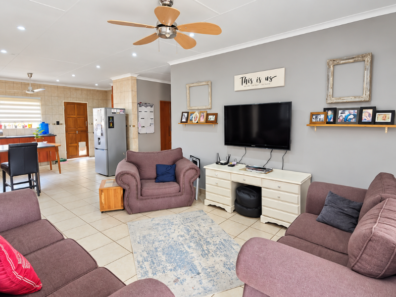 Spacious open-plan living area featuring tiled flooring, recessed lighting, and a ceiling fan, seamlessly flowing into a functional kitchen space.