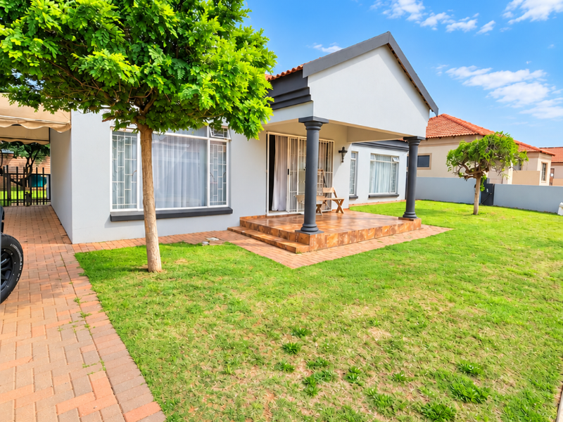 A well-maintained rear exterior view featuring a tiled patio, brick paved walkway, and a spacious lawn area.