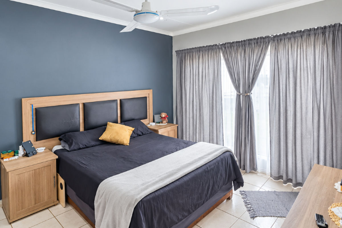 A well-maintained bedroom featuring tiled flooring, a ceiling fan, recessed lighting, and large windows with floor-to-ceiling curtains.