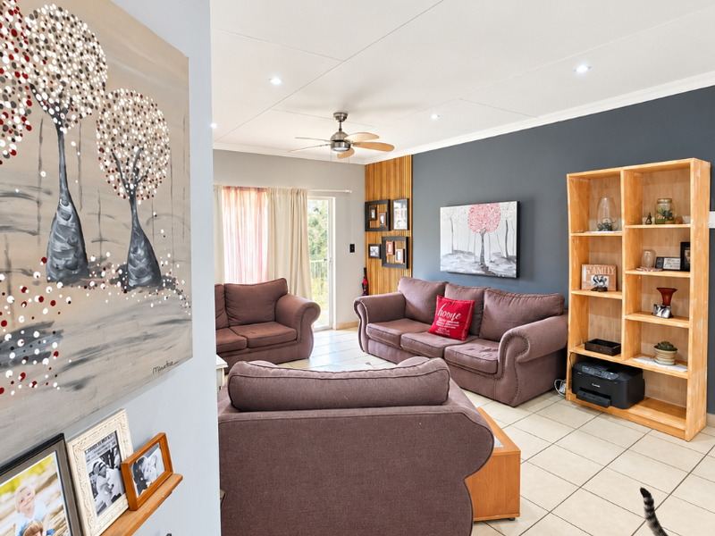 A spacious living room featuring neutral tiled flooring, a ceiling fan, recessed lighting, and a modern vertical timber slat feature wall.