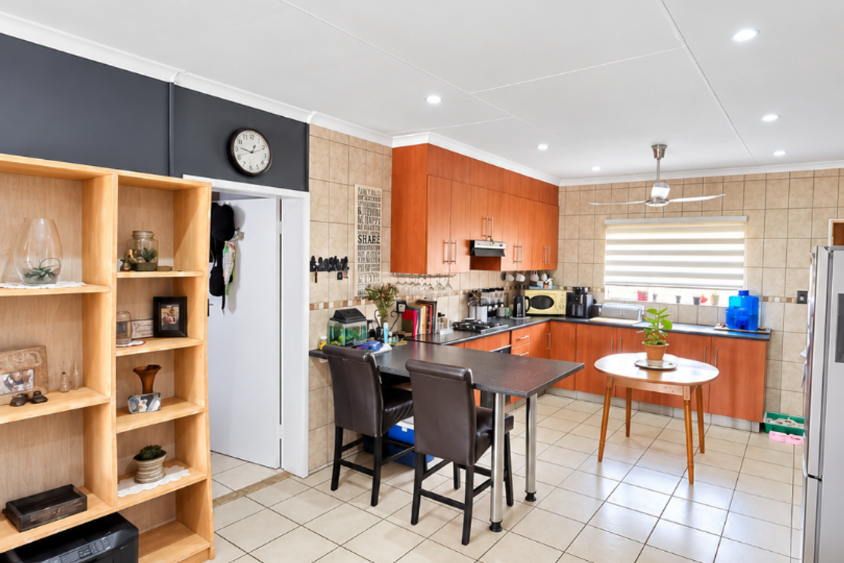 A functional kitchen featuring wooden cabinetry, tiled flooring, a tiled backsplash, and a built-in hob with an extractor fan.