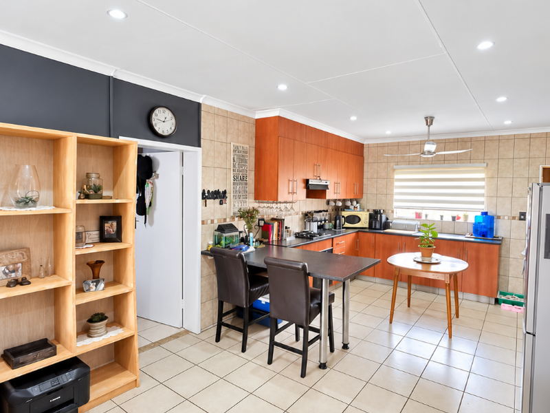 A functional kitchen featuring wooden cabinetry, tiled flooring, a tiled backsplash, and a built-in hob with an extractor fan.