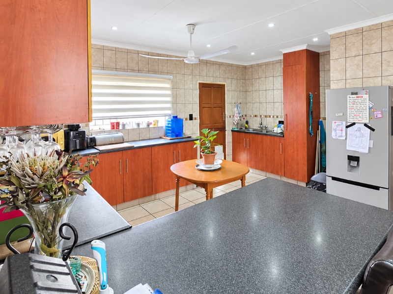 A functional kitchen featuring wood-look cabinetry, dark laminate countertops, tiled backsplash, and a central breakfast bar area with integrated sink and ceiling fan.