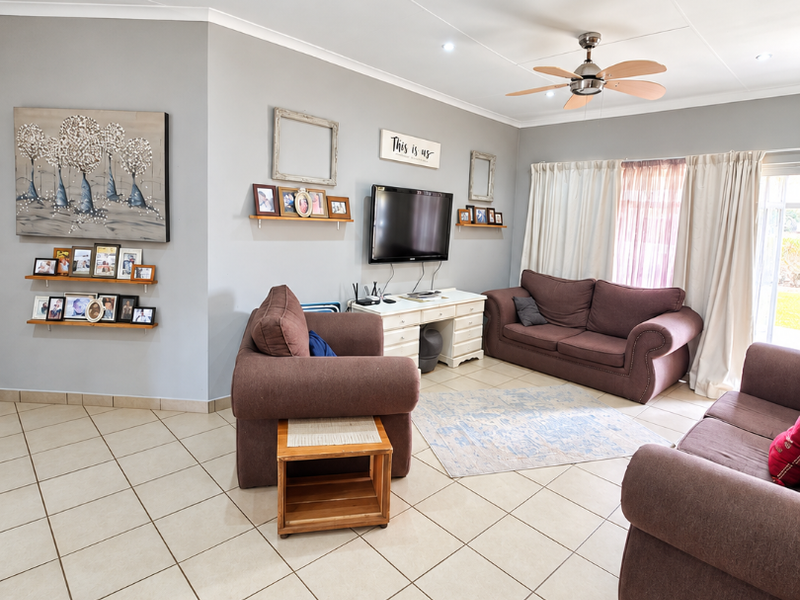 A spacious living room featuring neutral tiled flooring, a ceiling fan, recessed lighting, and access to the outdoors via a sliding glass door.