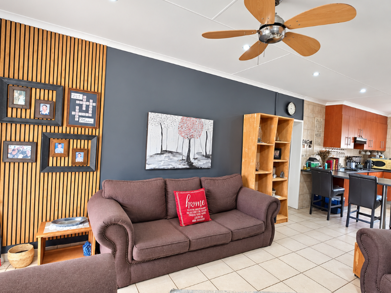 Open-plan living area featuring a timber slat feature wall, tiled flooring, recessed lighting, and a seamless transition to the kitchen with breakfast bar seating.
