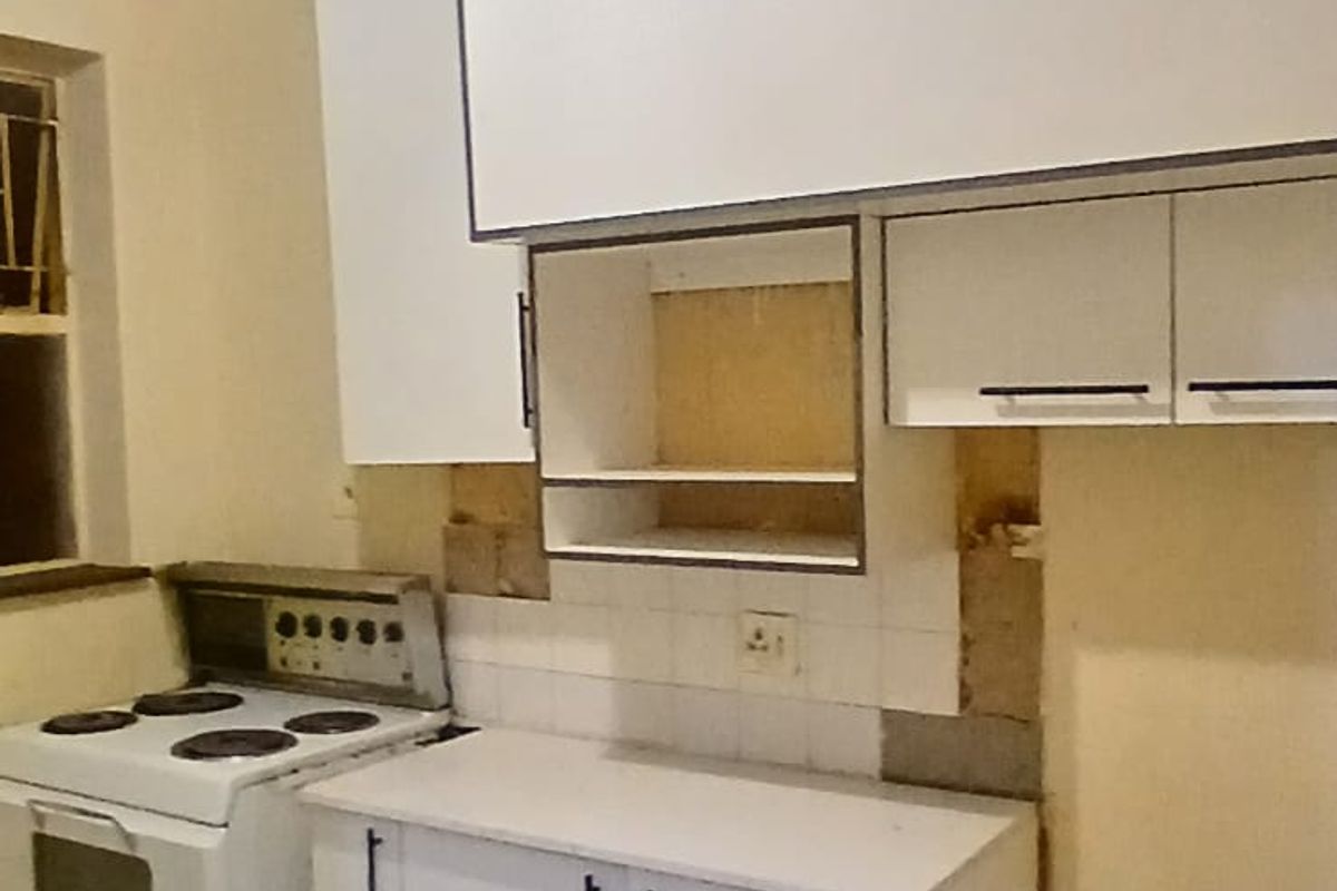 A kitchen area featuring white cabinetry and a freestanding stove, currently requiring completion of wall finishes and splashback tiling.