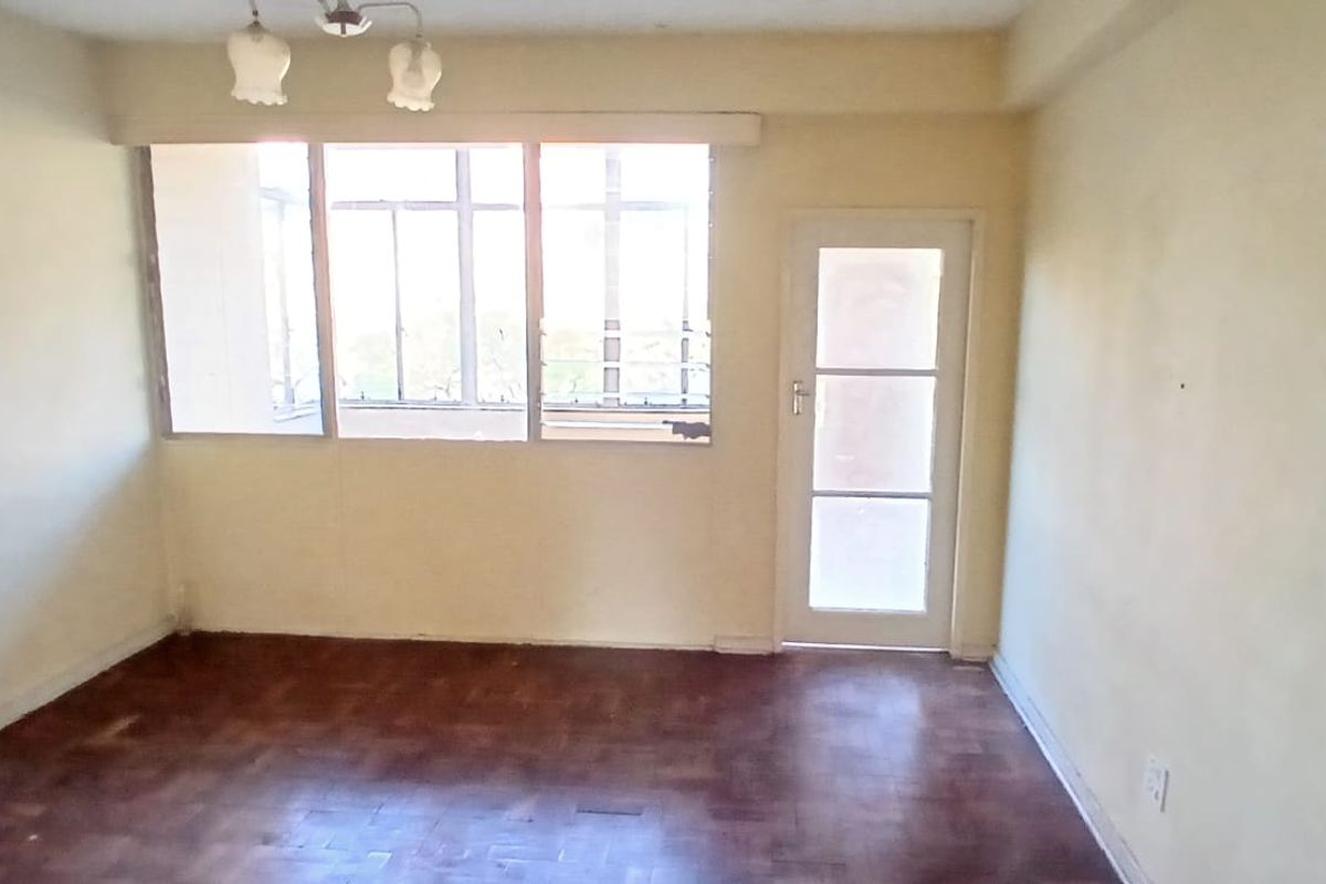 An empty living room featuring original parquet flooring, large windows, and a glass-paneled door leading to an adjacent space.