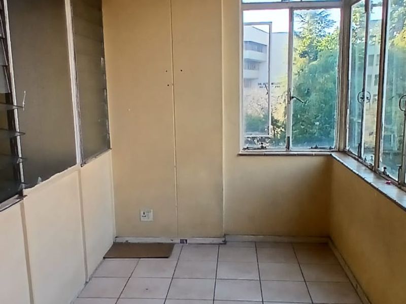 An enclosed balcony or sunroom featuring tiled flooring and large windows, offering a bright, versatile space ready for renovation or repurposing.