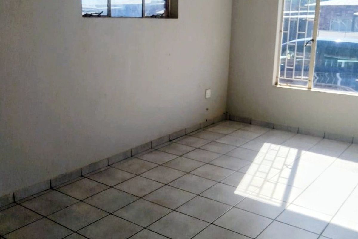 An empty living room featuring tiled flooring, natural light from two windows with security bars, and neutral wall finishes.