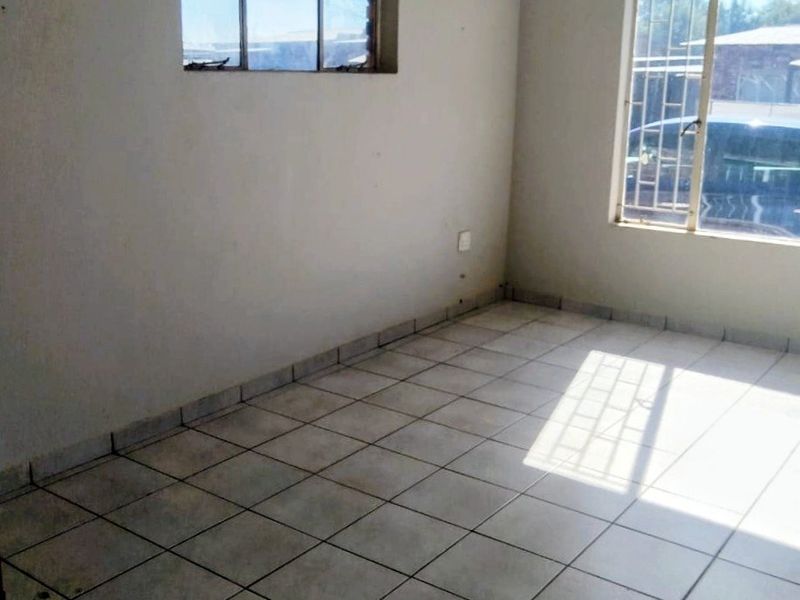An empty living room featuring tiled flooring, natural light from two windows with security bars, and neutral wall finishes.