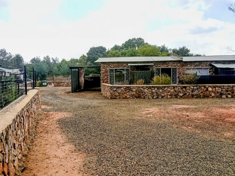 A view of the front exterior of the property featuring a gravel driveway, stone retaining walls, and a brick building with a metal roof.
